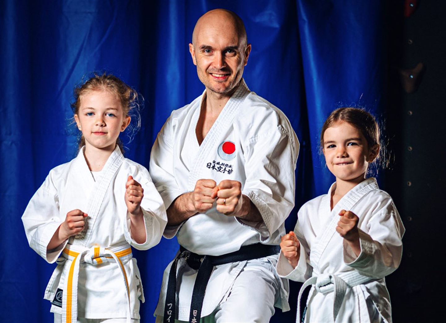 Mann og to jenter i karateutstyr.