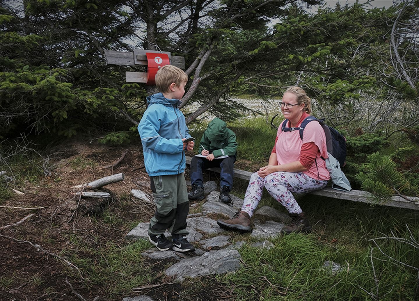 To barn og ei kvinne på tur i skogen.
