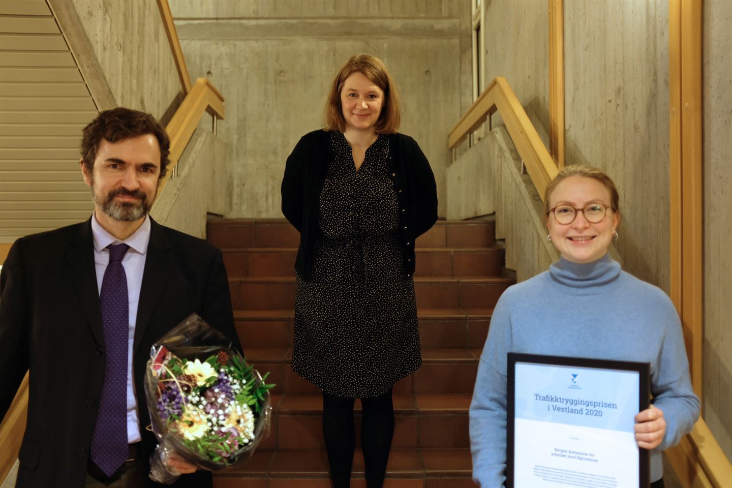 tre personar i trapp, en med blomsterbukett og en med diplom