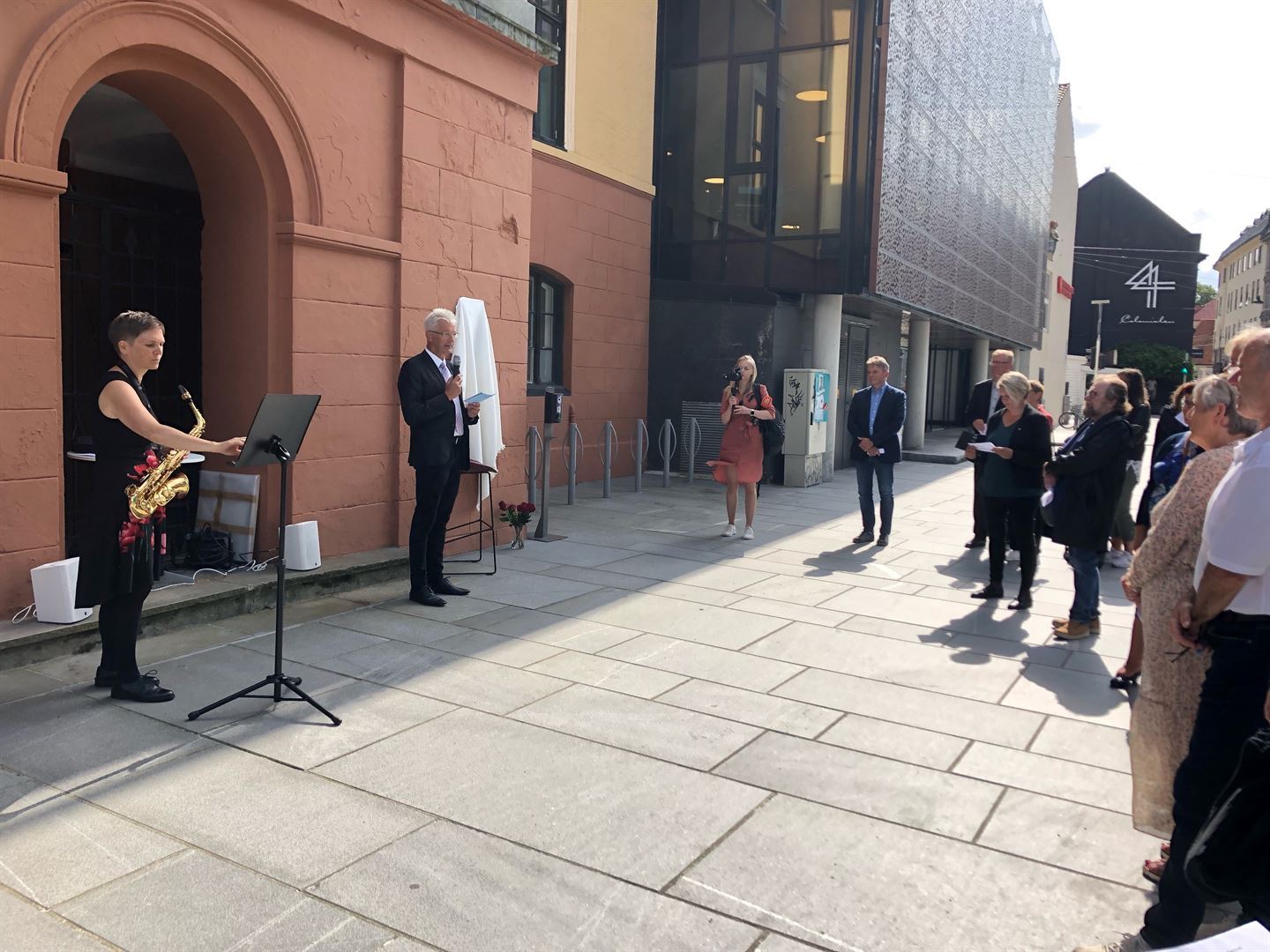 AVDUKA MINNEPLAKETT: Fylkesordførar Jon Askeland talar på markeringa der representantar for dei pårørande, fylkeskommunen, Bergen kommune, Bergen Katedralskole og AUF/Arbeiderpartiet deltok. Saksofonist Yvonne Jasmine Demirel spelte «Til ungdomen». Foto: Anbjørn Holme, Vestland fylkeskommune.