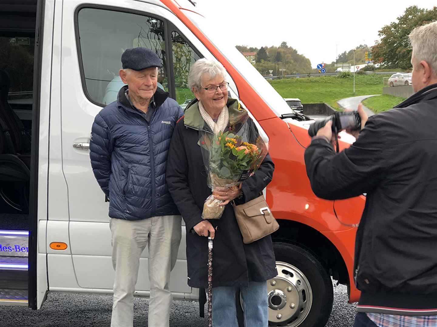 foto av to menneska framfor buss med blomsterbukett