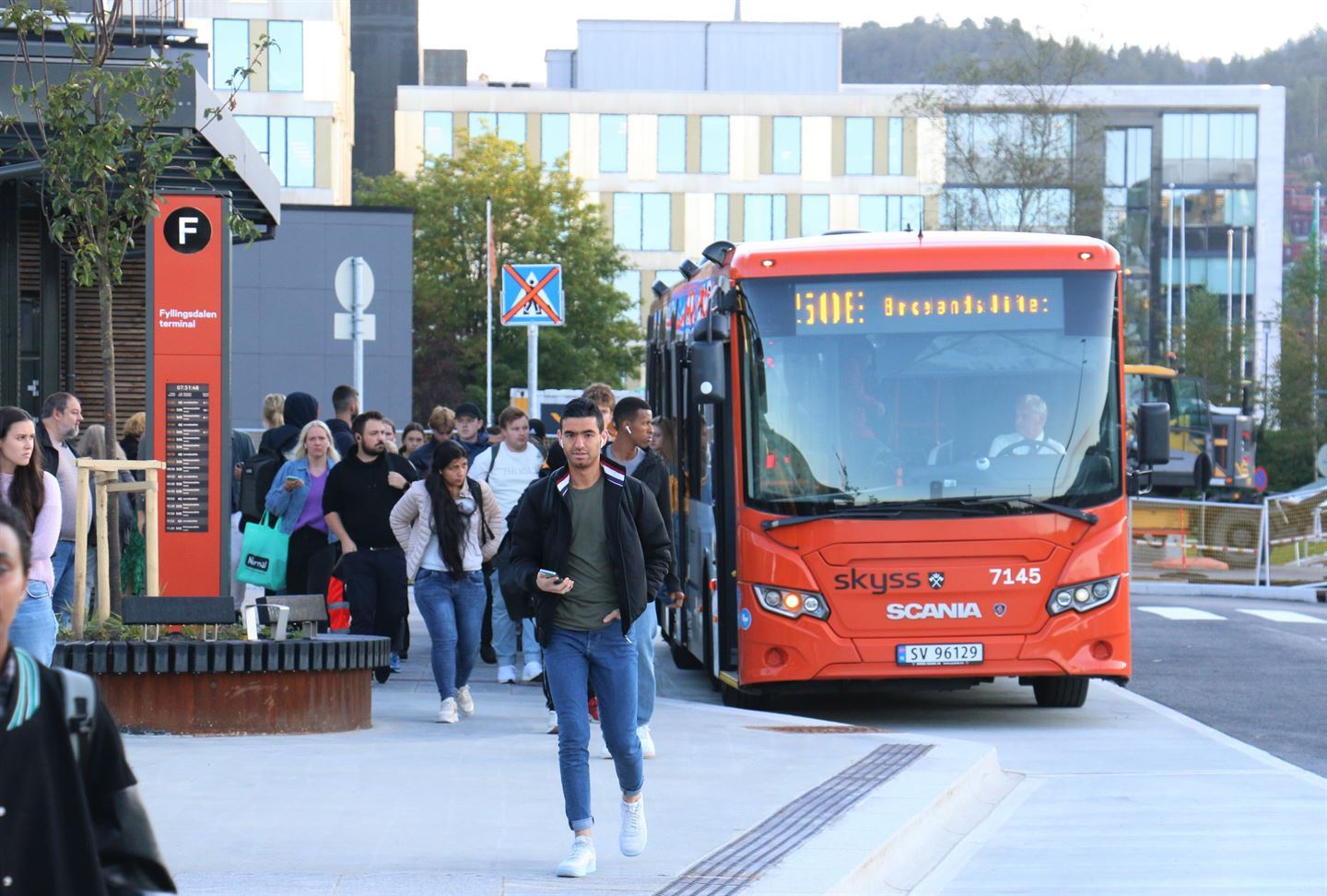 Buss som er parkert og mange reisande som går på gangvegen. Foto.