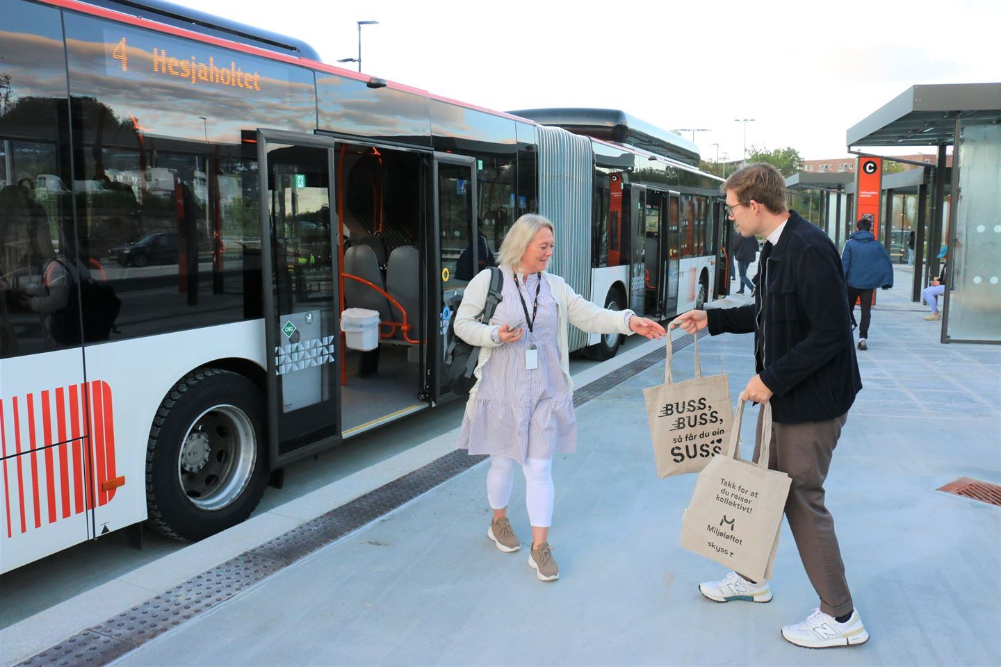 Kvinne utanfor buss med handlenett med slagordet til Skyss. Foto.