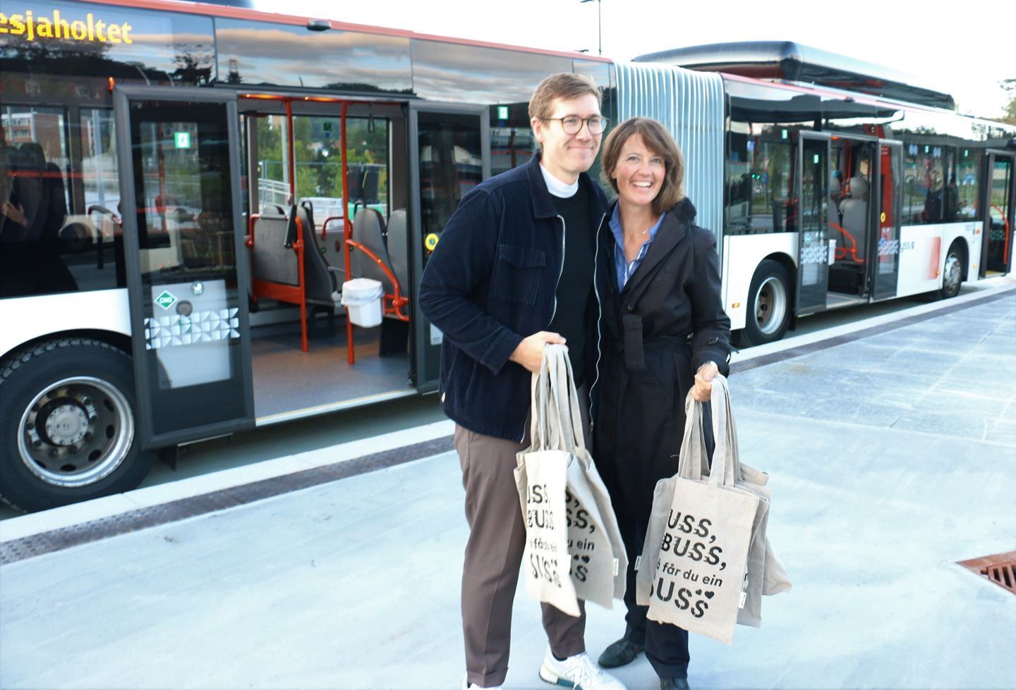 Kvinne og mann med handlenett utanfor buss. Foto.