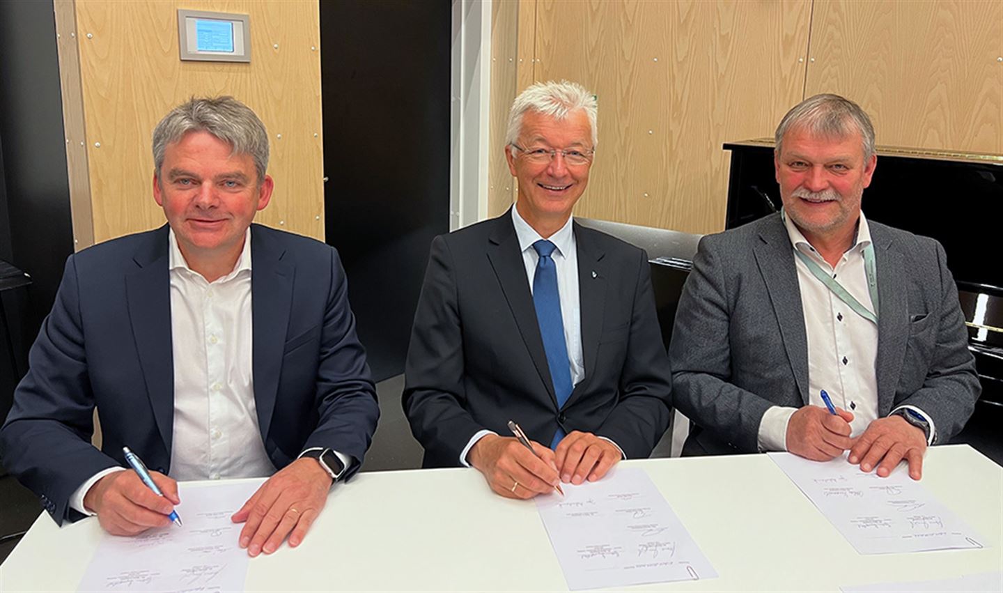 Tre menn signerer eit papirdokument. Foto.