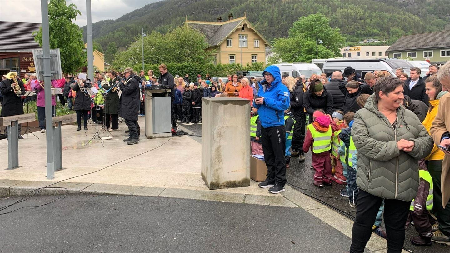Korps som spelar utandørs, bygdefolke som publikum. Foto.