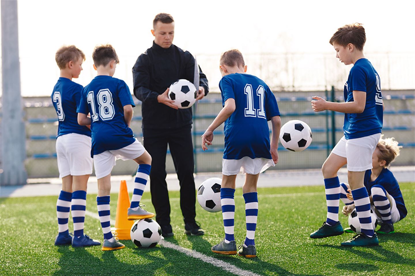 foto av ungar i fotballdrakt som står rundt ein trenar