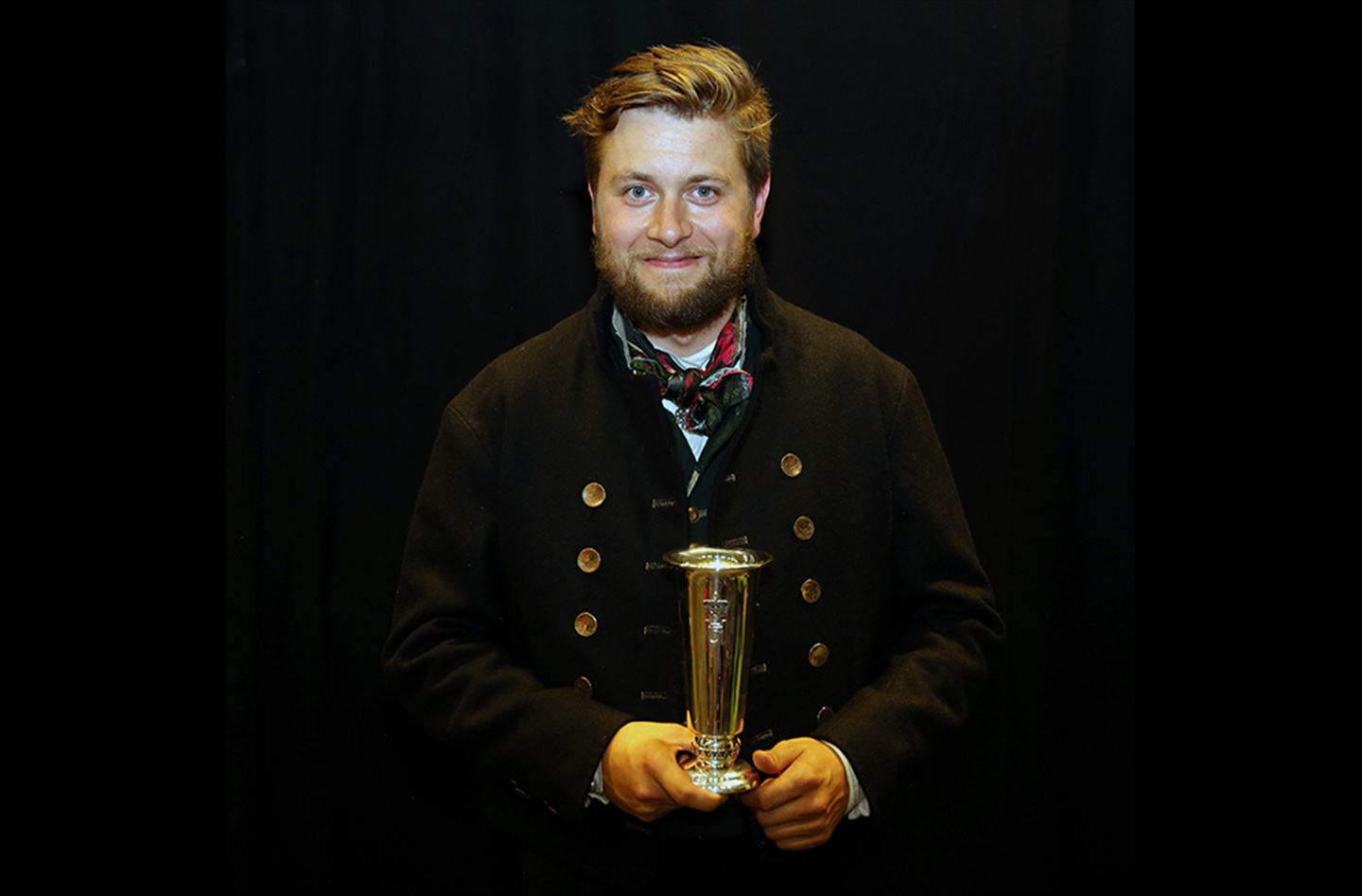 foto av mann i bunad som held kongepokal
