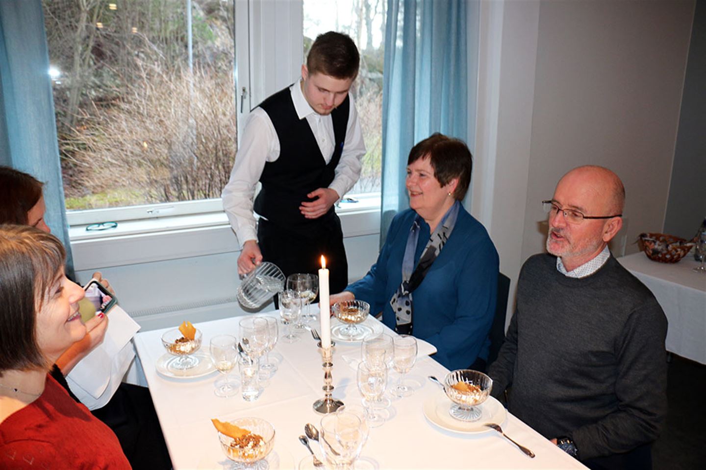 Servitør som fyller vatn i glas til gjestene. Foto.