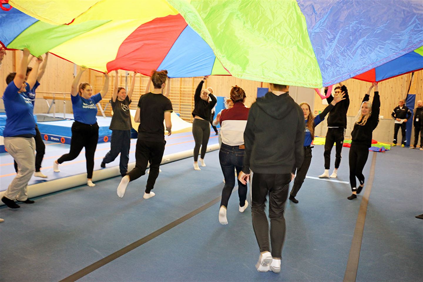 Ungdommar i gymtime, står i ring og held eit stort fargerikt flagg. Foto.