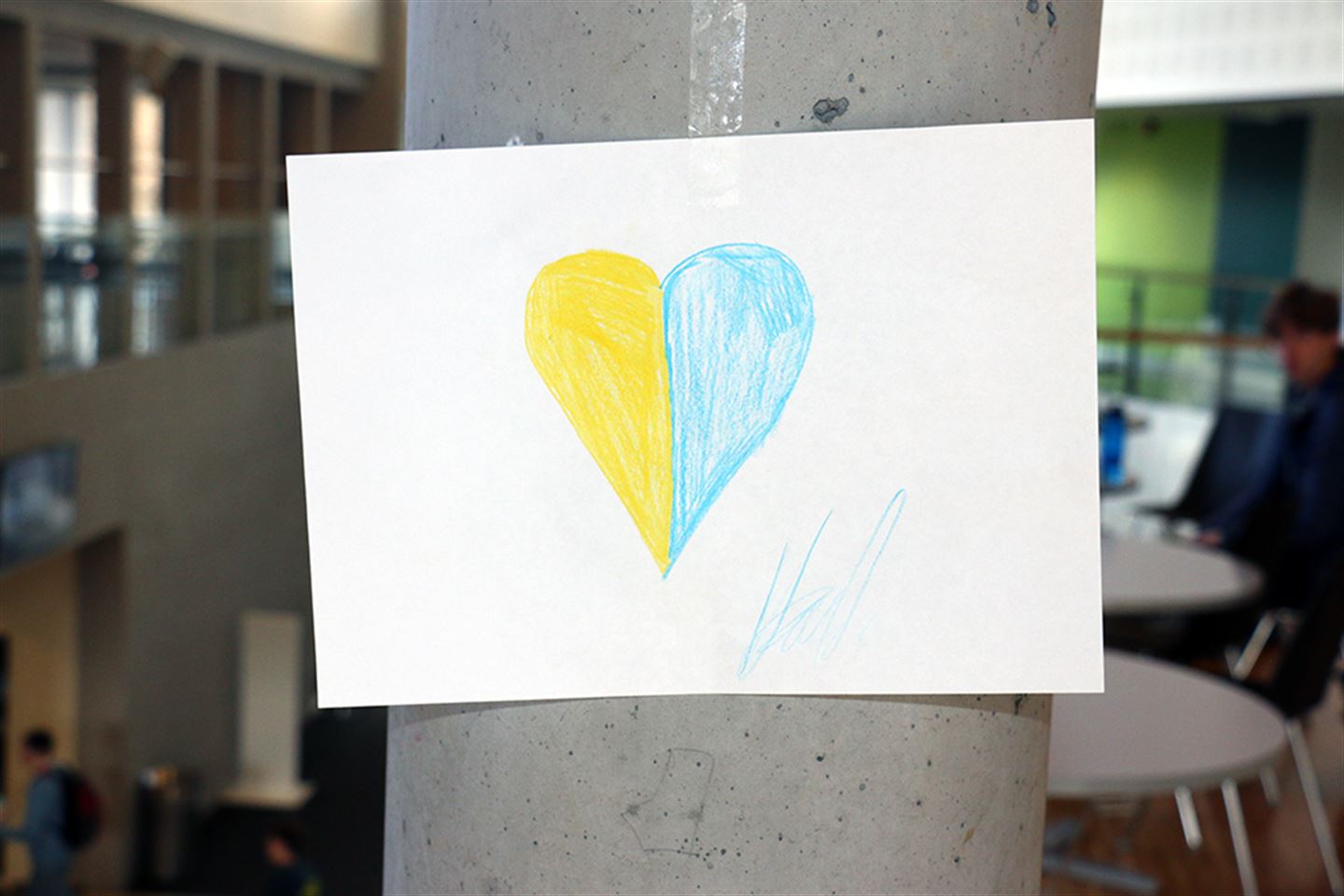 Eit a4 ark som er teikna eit blått og gult hjerte på er hengt opp på ei betongsøyle. Foto. 