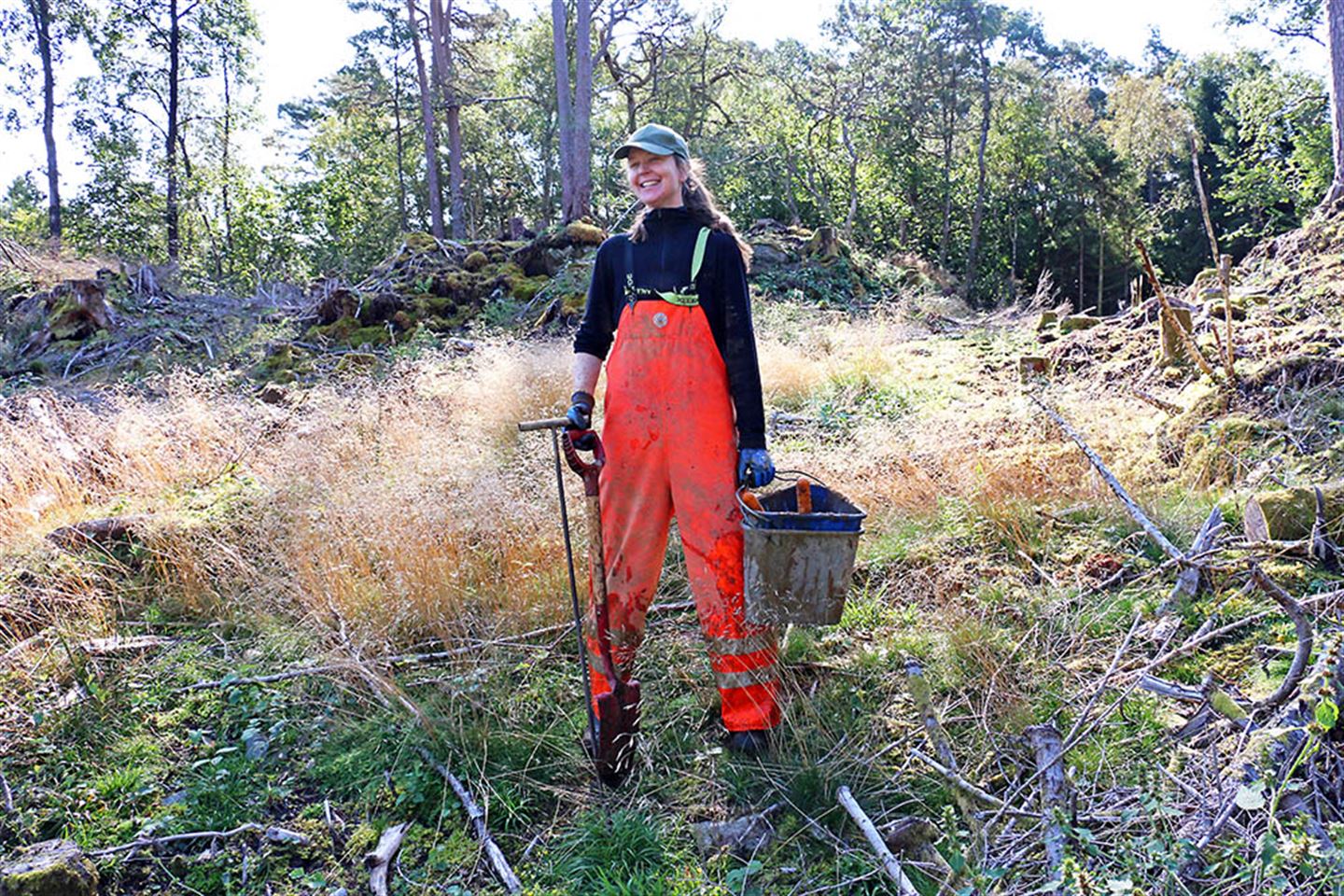 Person ute i ope terreng med spade og bøtte.