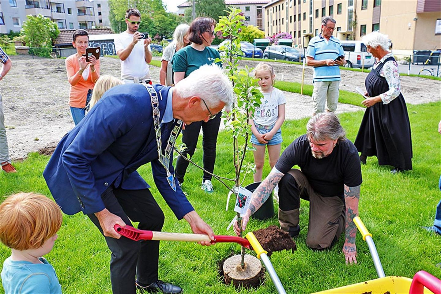 To personar plantar epletre, mens fleire står rundt og ser på.