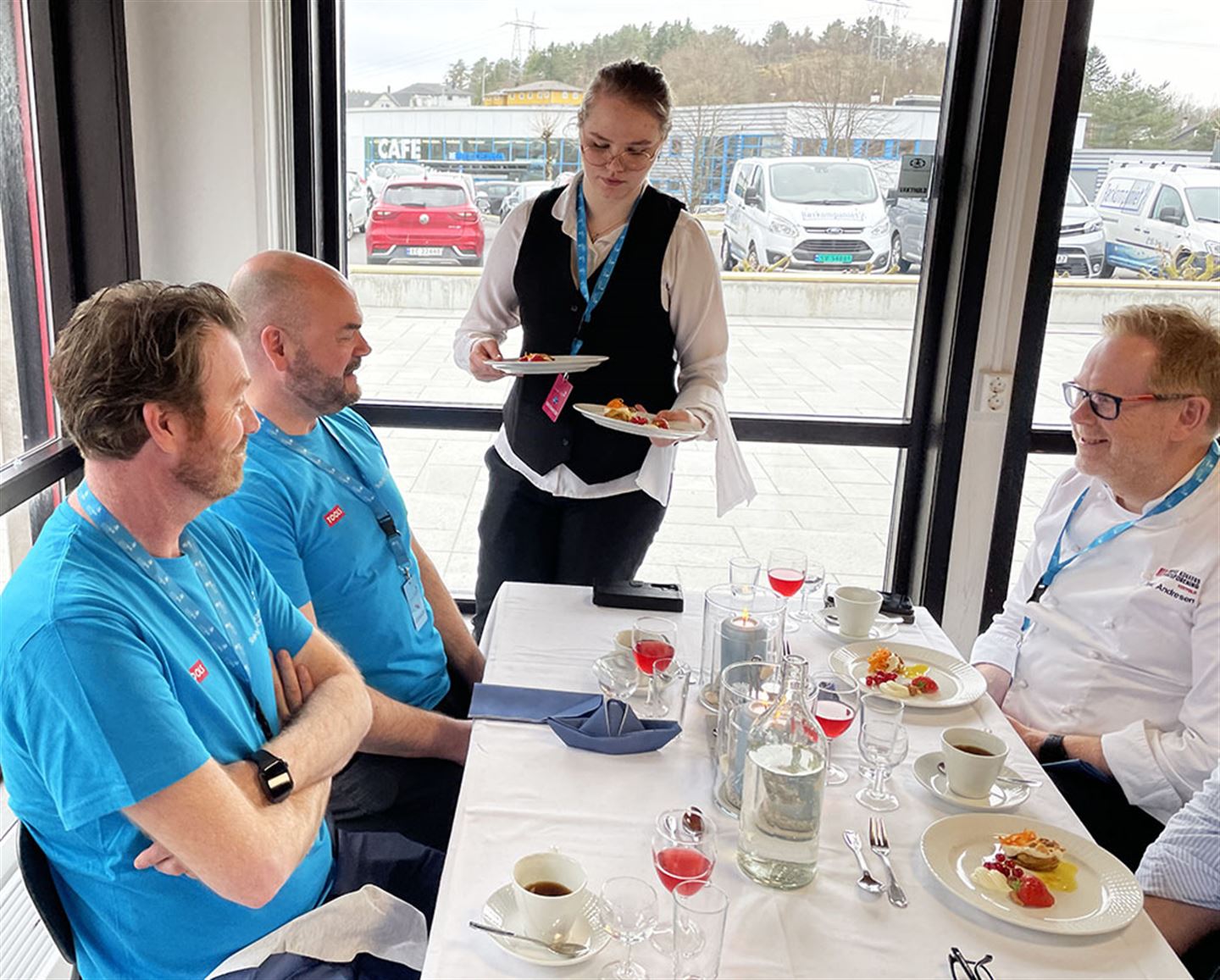 Jente serverer mat ved bord med tre personar.