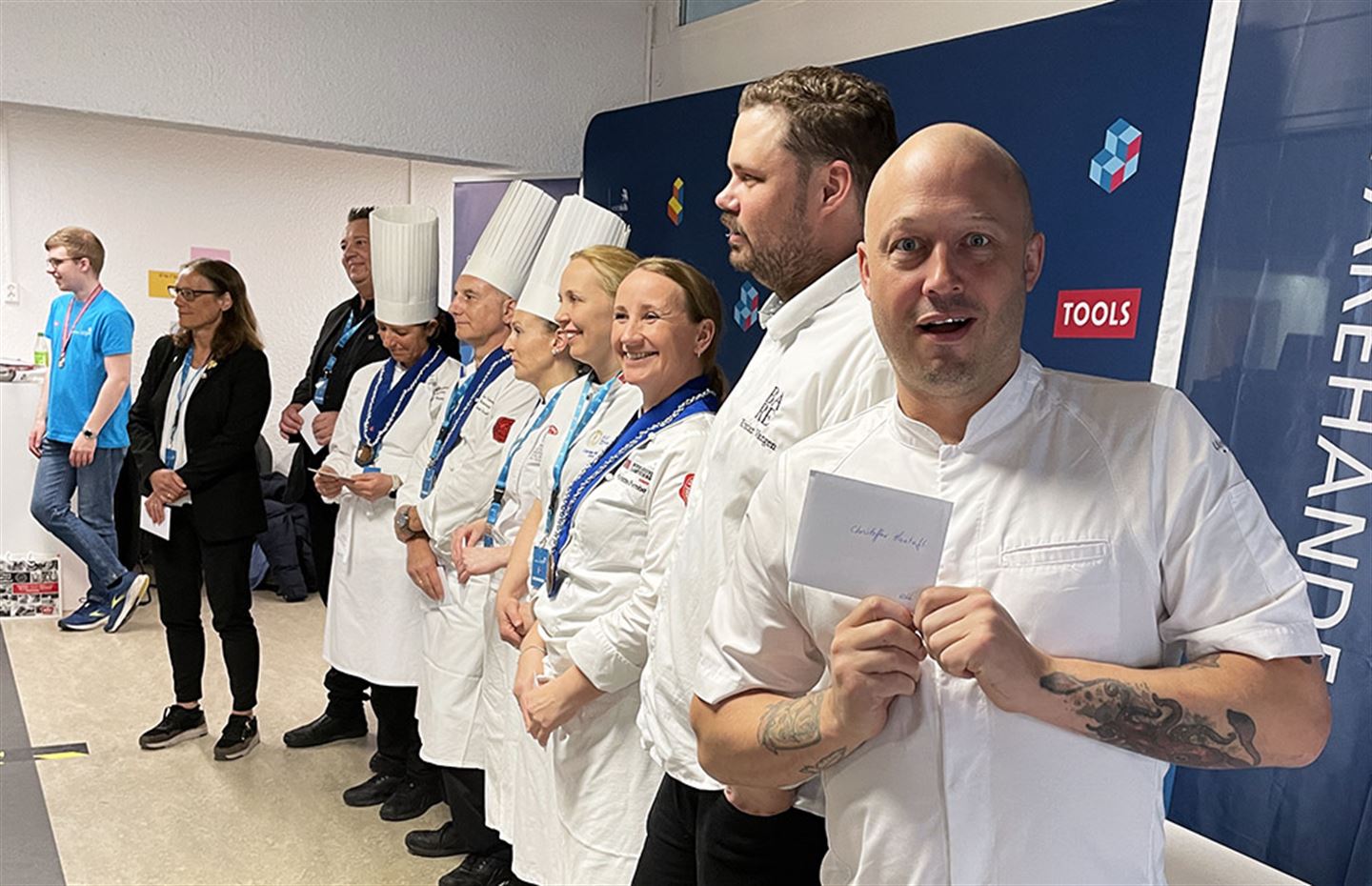 Menn og kvinner i kokkeuniform oppstilt på rekke.