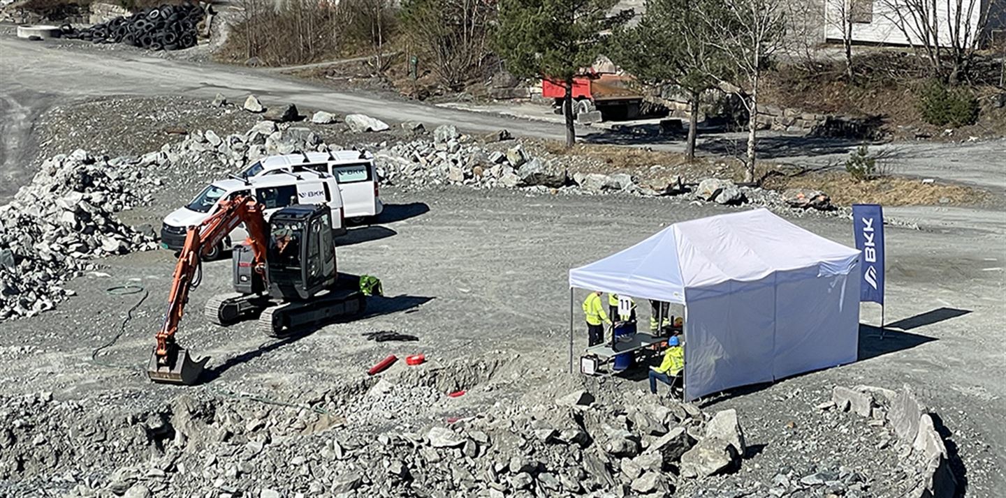 Anleggsplass med gravemaskin som grev nær høgspentkabel.