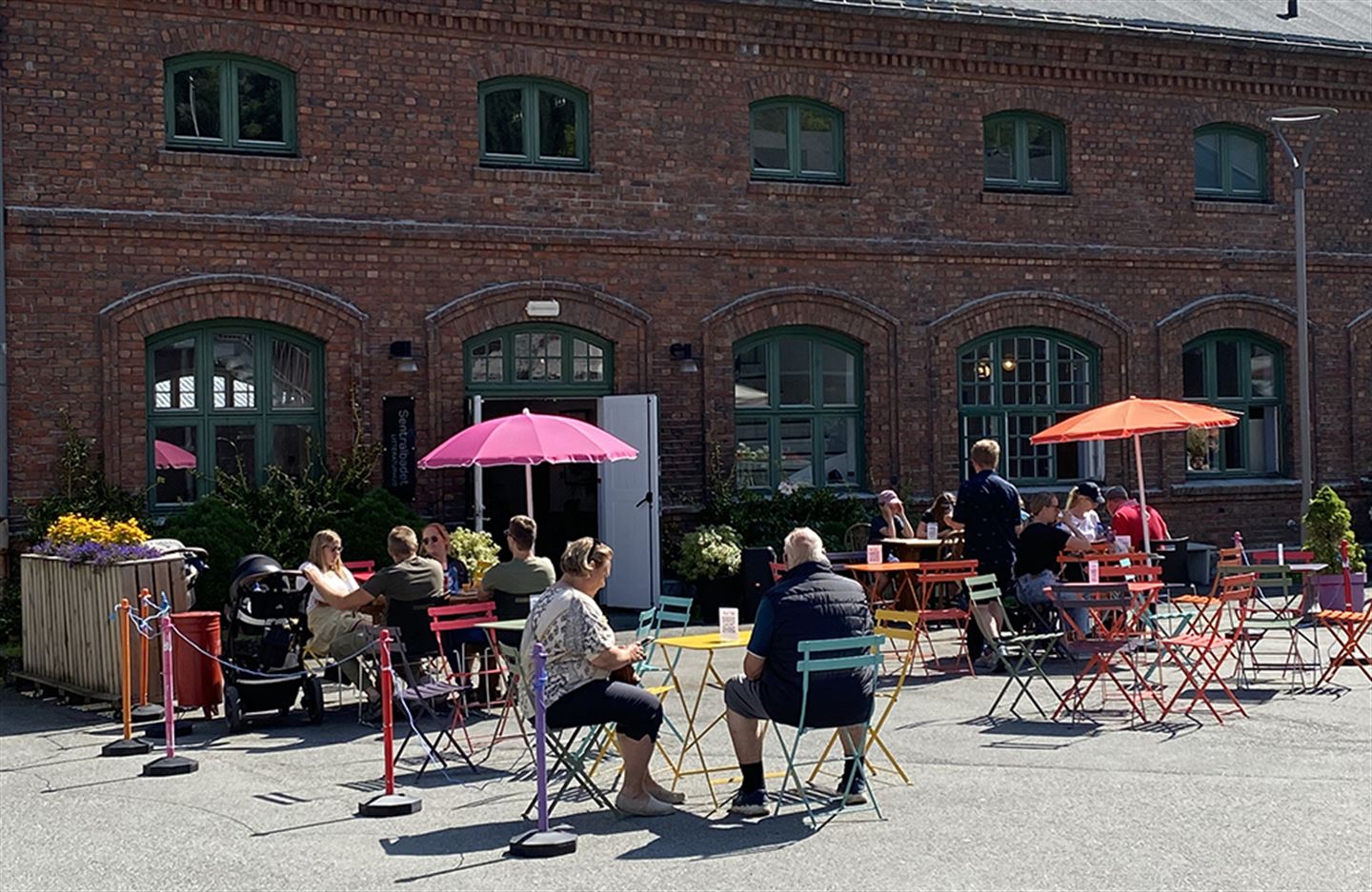 Menneske som sit ved små kafébord utanfor murbygg.