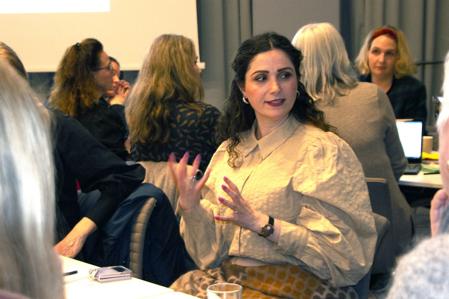 bilde av Nooshin Zaery Loolani frå som sit ved eit bord i lag med andre i eit stort møterom. Ho er engasjert i diskusjon og gestikulerer med hendene og ser mot sin venstre. Langt mørkt hår og iført gul bluse.