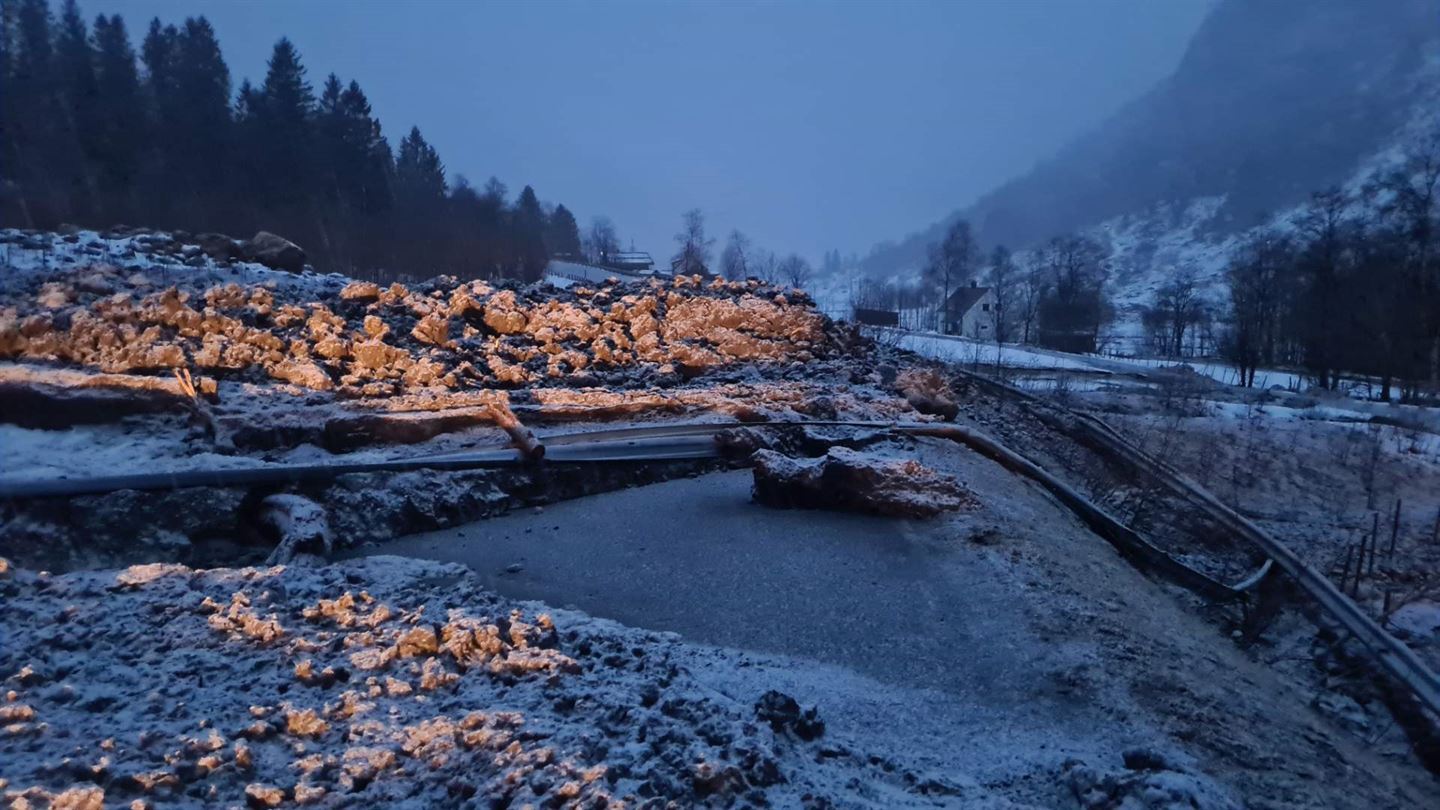 jord- og snøskred over fylkesveg, massar med snø på ligg over vegen, øydelagd autovern ligg over vegen, det er halvmørkt og vinter. gråvêr. 