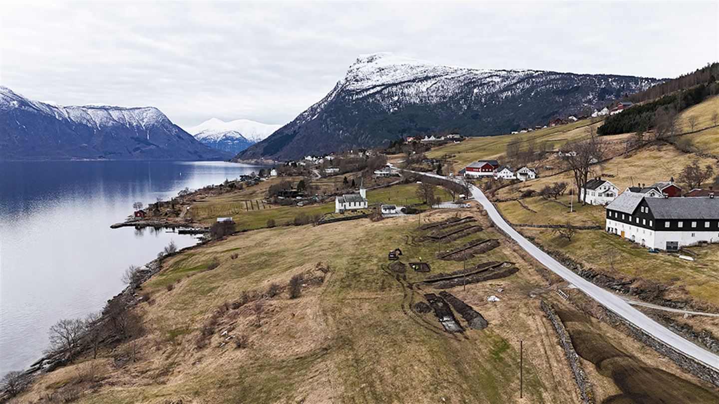 Dronebilde av fylkesveg langs fjord. Langs vegen ser vi sjakter for arkeologiske registreringar.