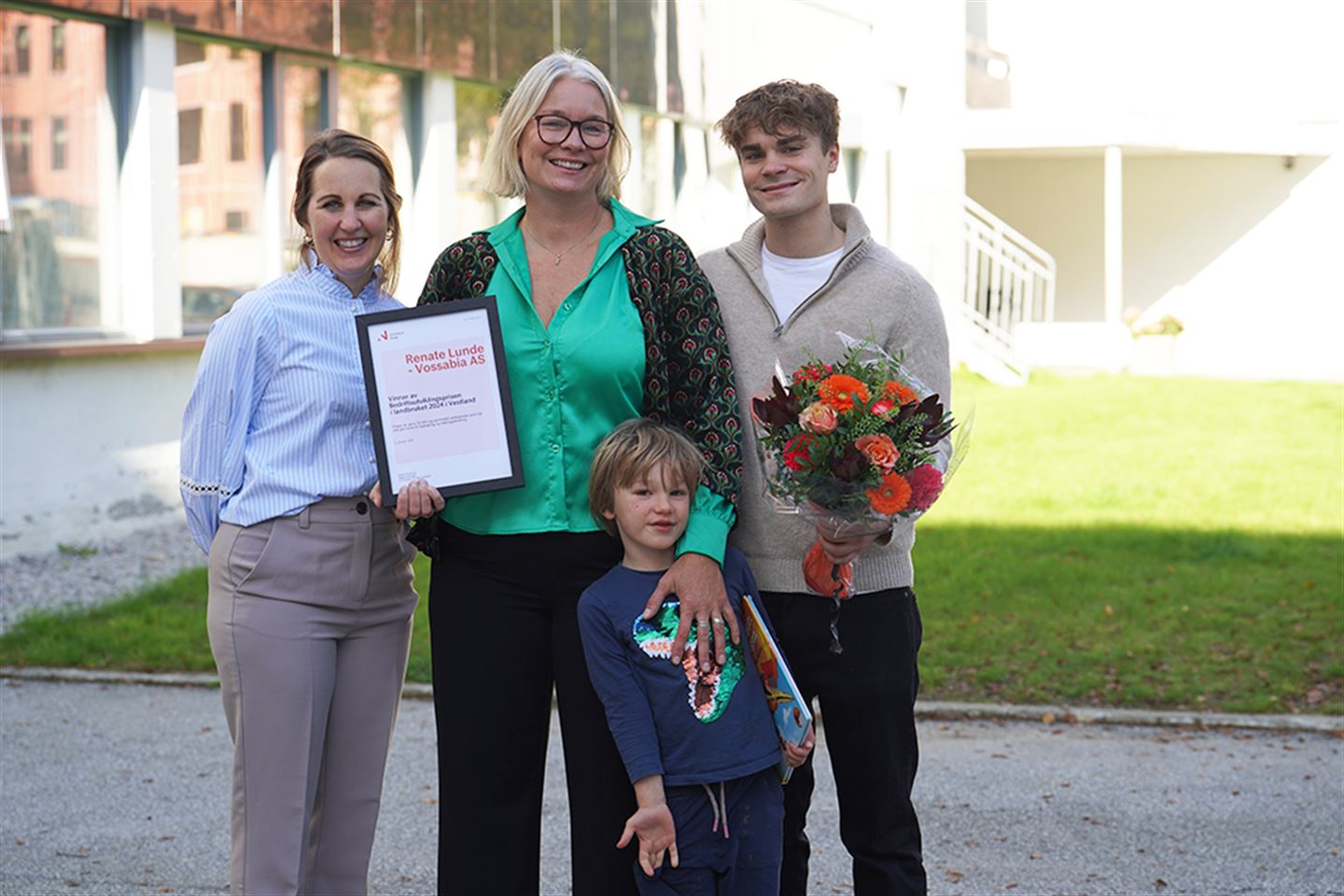 To kvinner, ein ung gut og ein liten gut. Ei av kvinnene held blomsterbukett og diplom.