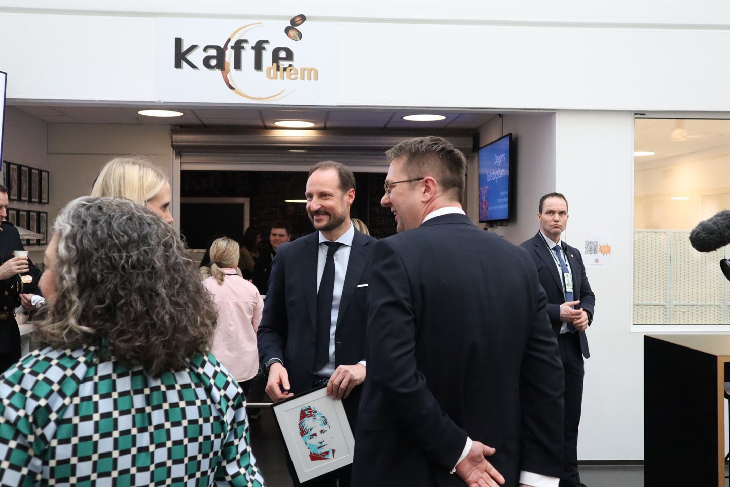Kronprins Haakon kledd i dress snakker med to personer