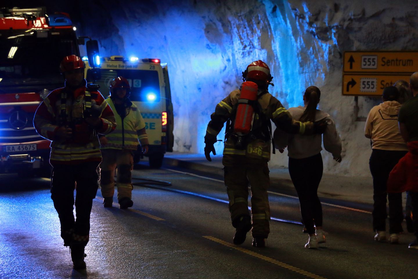 Ein raud brannbil og ein gul ambulanse med blålys på inni ein tunell. I vegbana går brannmenn og ambulansepersonell med skadde frå ei ulykke. Foto: Silje Alvsaker/Vestland fylkeskommune