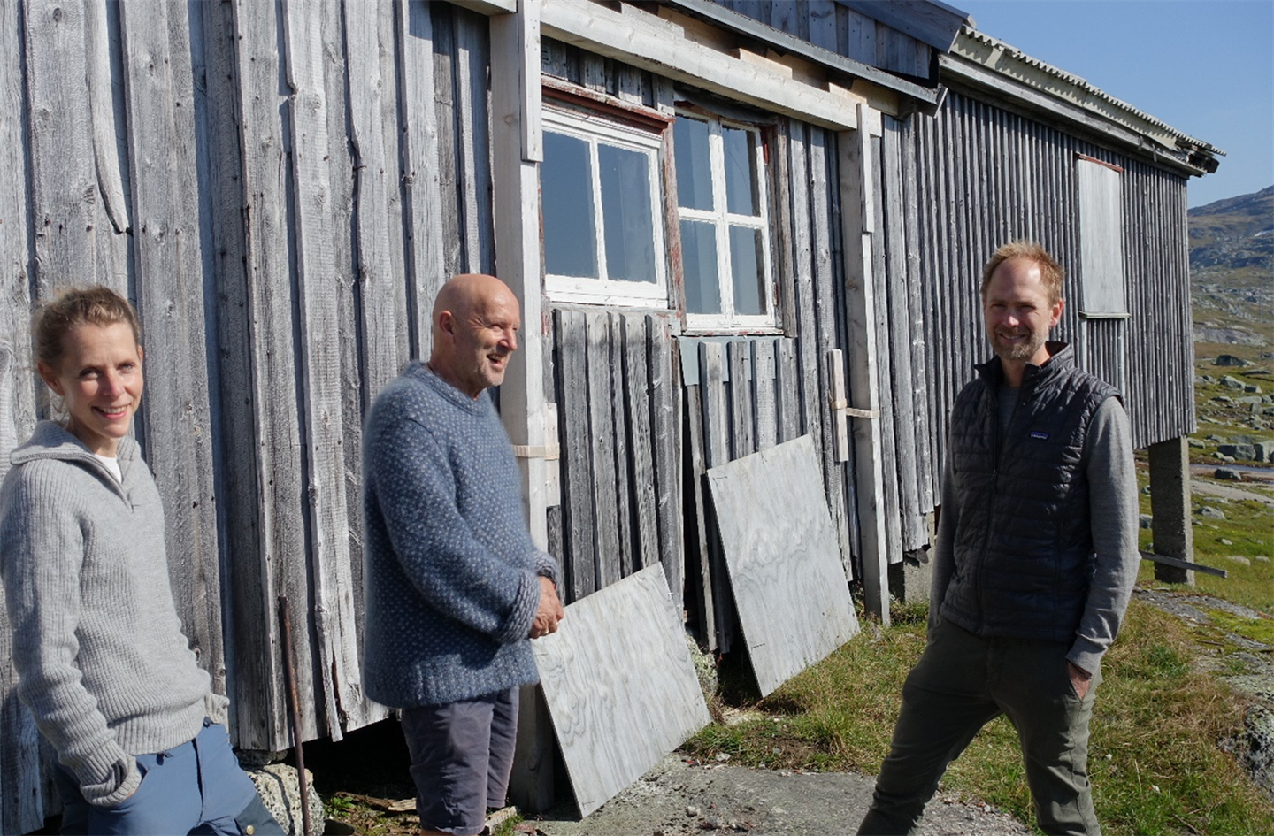NYE EIGARAR: Hausten 2023 skifta Slirå rallarbrakke eigar. Dei nye eigarane er Ragna Os Eskeland (til venstre) og Sondre Gundersen (til høgre). Dei har fått økonomisk tilskot av Vestland fylkeskommune til sikring og istandsetting av brakka. Tømrar Bjørn Vike i midten. (Foto: Øystein Monsen, Vestland fylkeskommune)