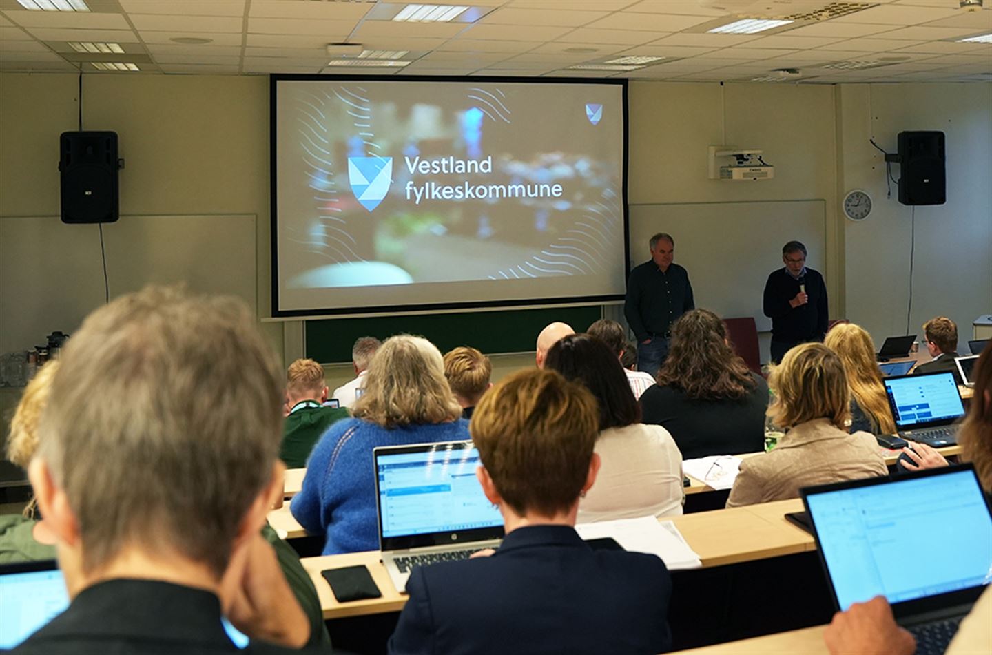 Personar samla i auditorium med skjerm med teksten Vestland fylkeskommune fremst.