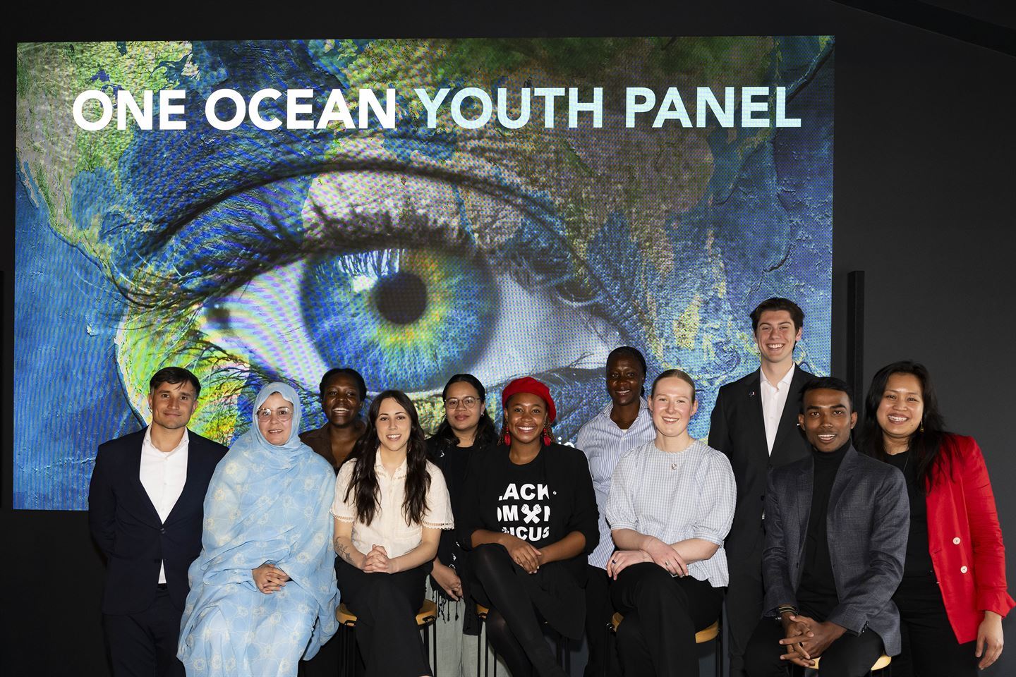 Elleve unge menneske sit foran ein skjerm. På skjermen er det bilde av eit fjes med auge i fokus. Fjeset er i fargene til jordkloden. På skjermen står det One ocean youth panel med kvit skrift. Foto: Thor Brødreskift