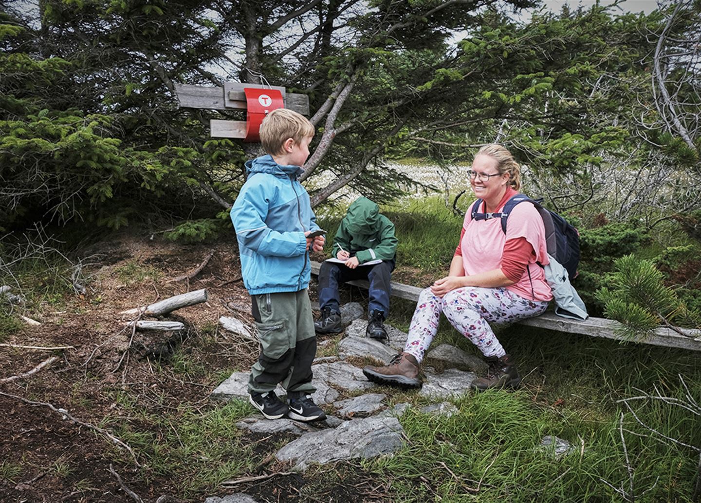 Kvinne og to barn ute i naturen ved raud postkasse med T på.