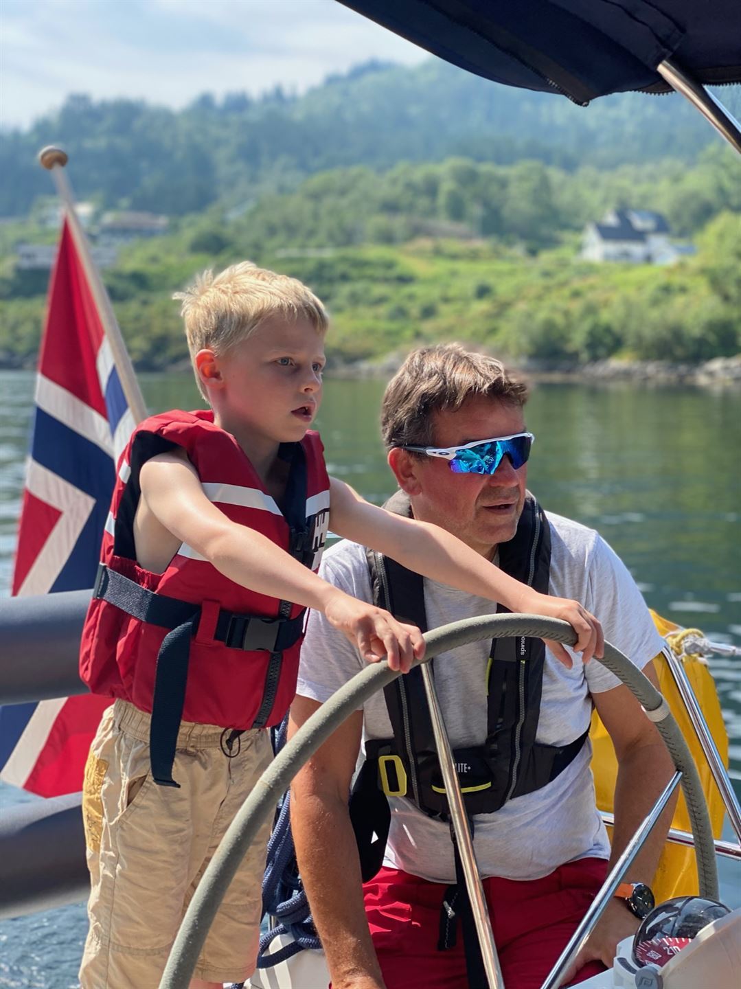 foto av barn og vaksen mann ved roret på ein seglbåt