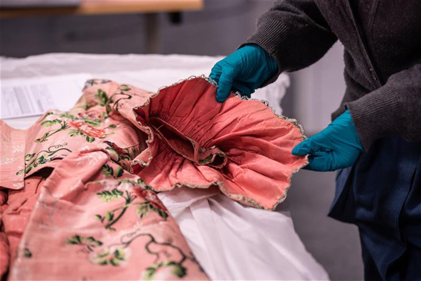 Hender som jobbar med gamal rosa brokadekjole.