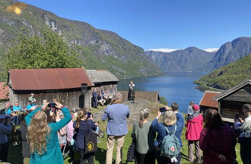Kvinne spelar lur på Otternes i Aurland, framfor publikum. Utsikt over Aurlandsfjorden.