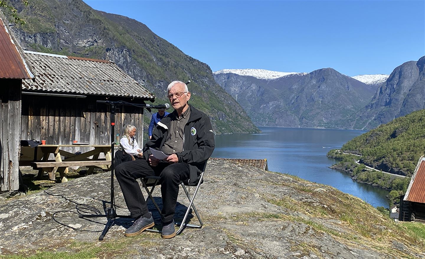 Eldre mann sitjande på ein stol ute på gamalt tun.