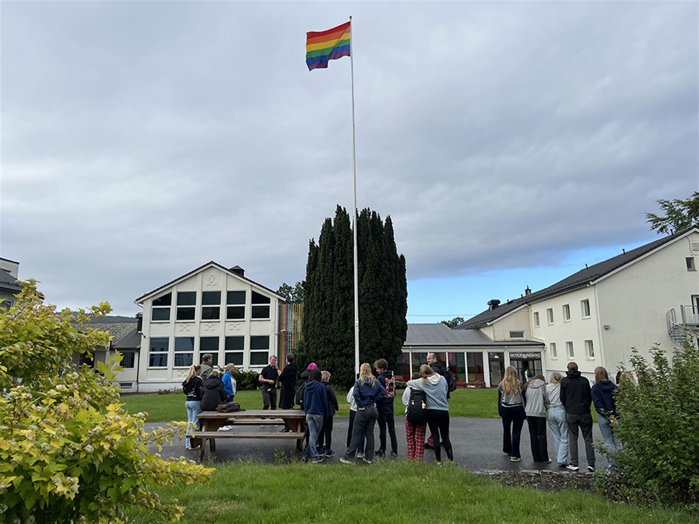 Ungdomar samla rundt flaggstang, der regnbogeflagget er heist.