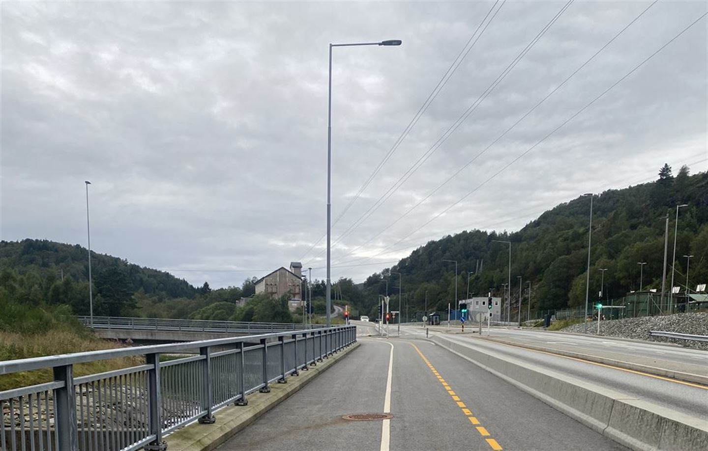 Grå asfalt på gang og sykkelveg. i midten er ei kvit stripe, til høgre er ei gul stripe. Betongklossar skil gang og sykkelvegen frå bilvegen som er heilt til høgre i bildet. 