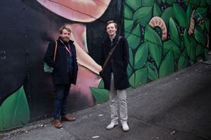 foto av to personar foran ein fargerik vegg