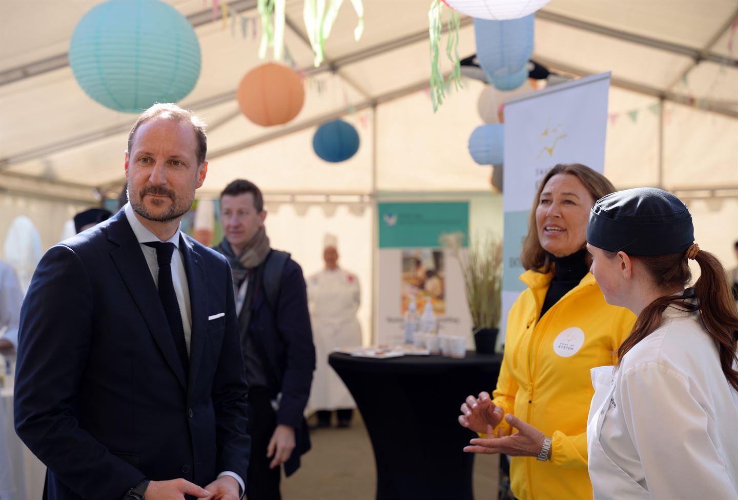 foto av kronprins haakon som snakkar med tre andre personar