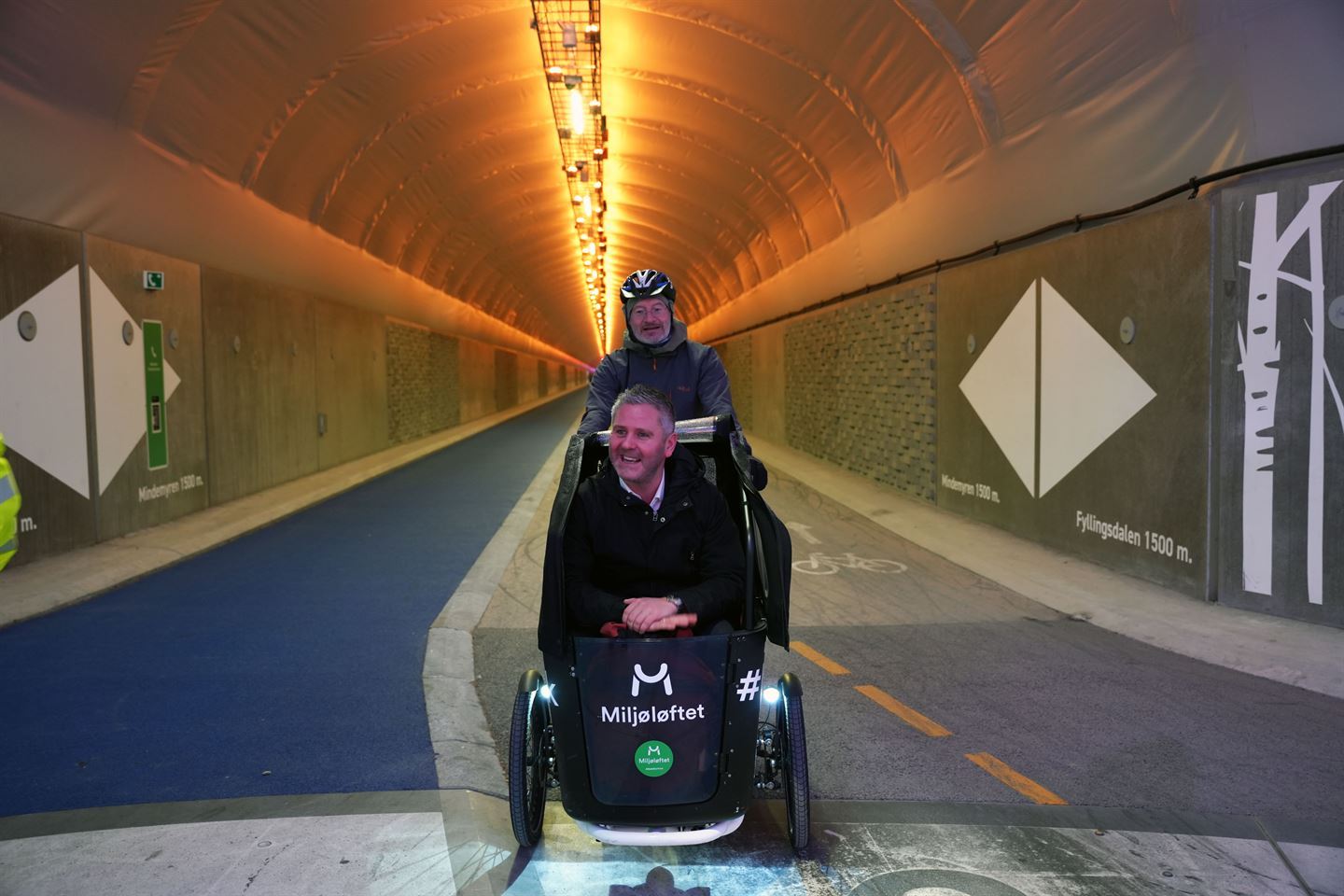 Ein mann på sykkel som fraktar ein annan mann som sit foran. 