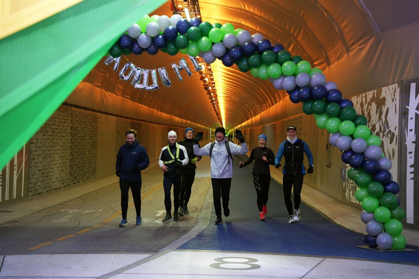 Joggarar i ein tunell. Dei løper gjennom ei ballongboge. 