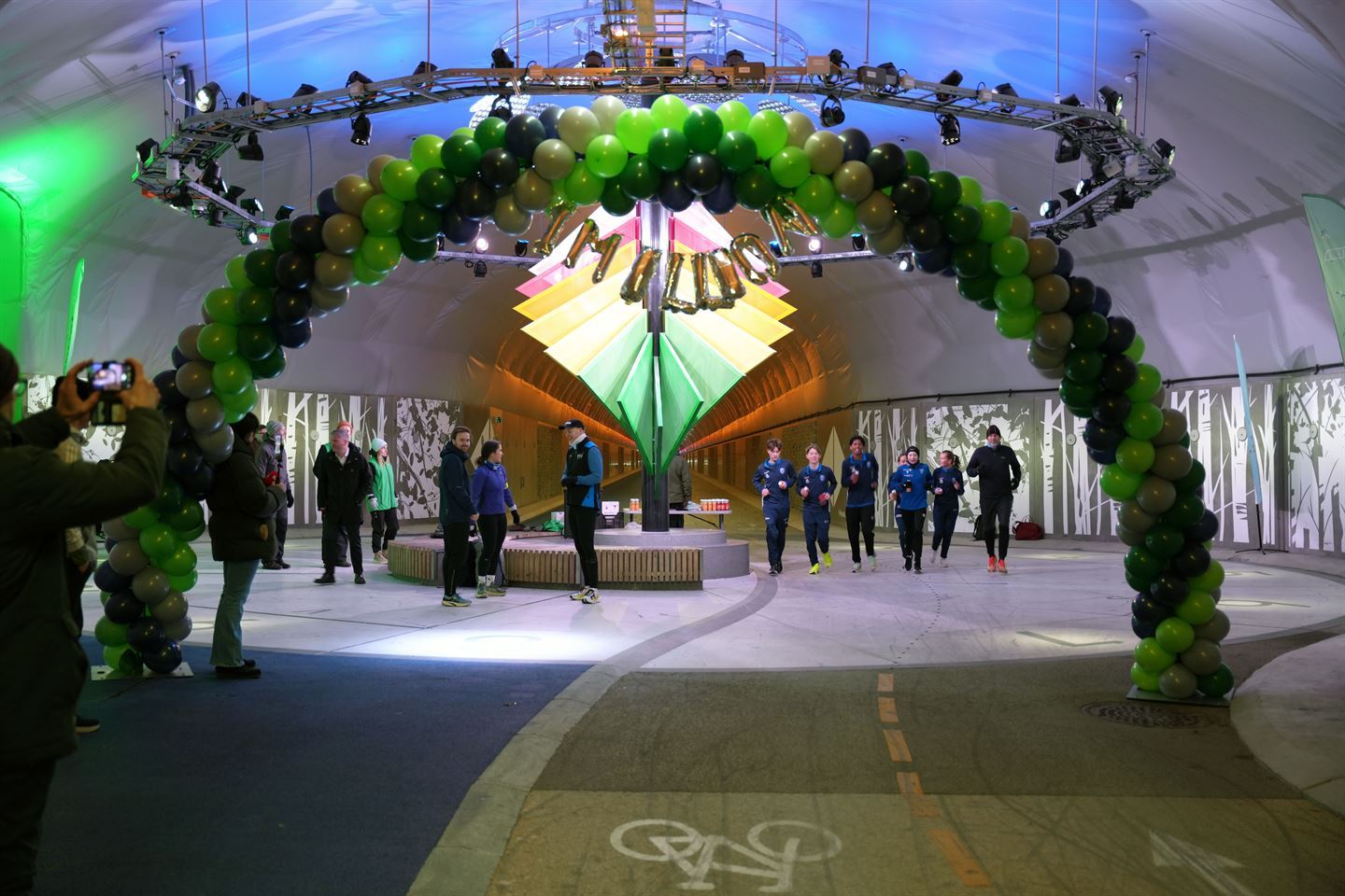 Mange menneske i ein tunell der dei kan sykle og gå. Eit lag trener med å løpe gjennom tunellen. 