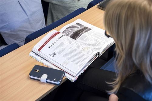 Jente leser i en bok med en mobil ved siden av boken