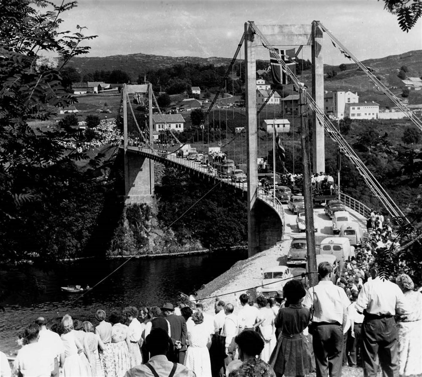 Svart-kvitt bilde av ei gamal bru. Det står mange mennesker og ser på bilane som køyrer over bru. 