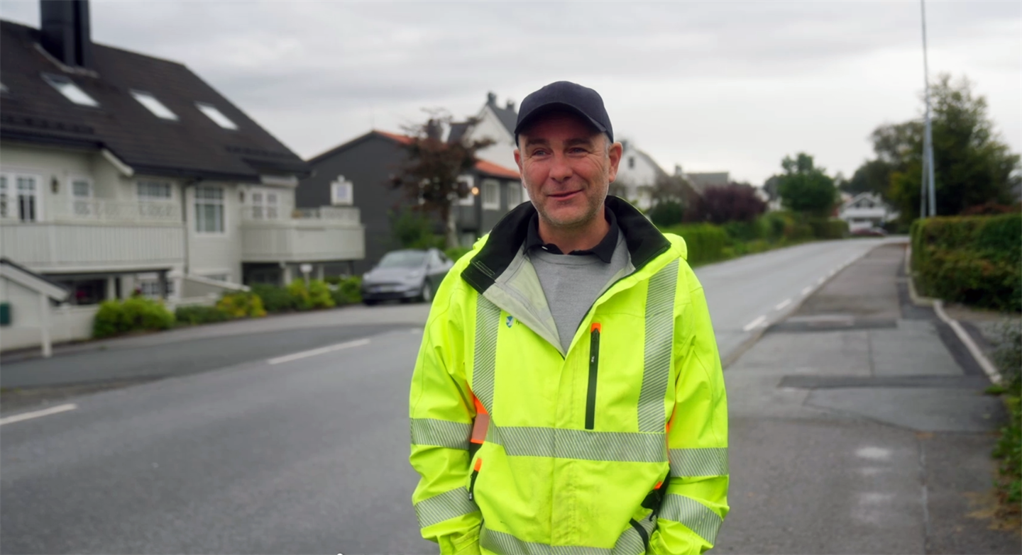 Ein mann i ei gate med refleksjakke i gult og mørk caps på hovudet. 