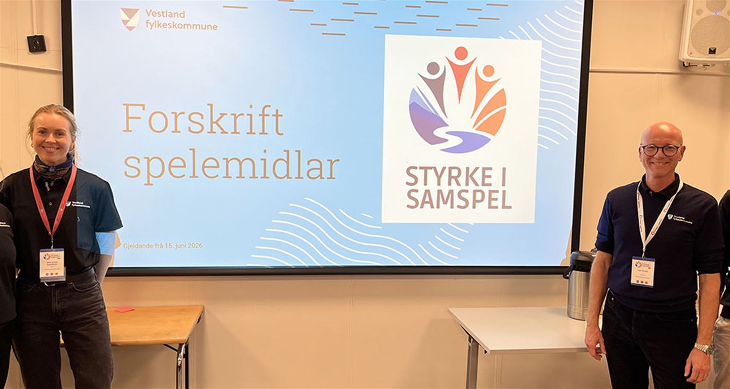 Ei kvinne og ein mann framfor ein skjerm med teksten Forskrift spelemidlar - Styrke i samspel.