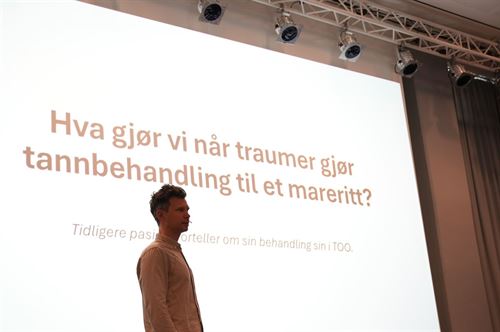 Psykolog John tveit-winther står i en konferansesal, foran en storskjerm der det står "hva gjør vi når traumer gjør tannbehandling til eit mareritt?"