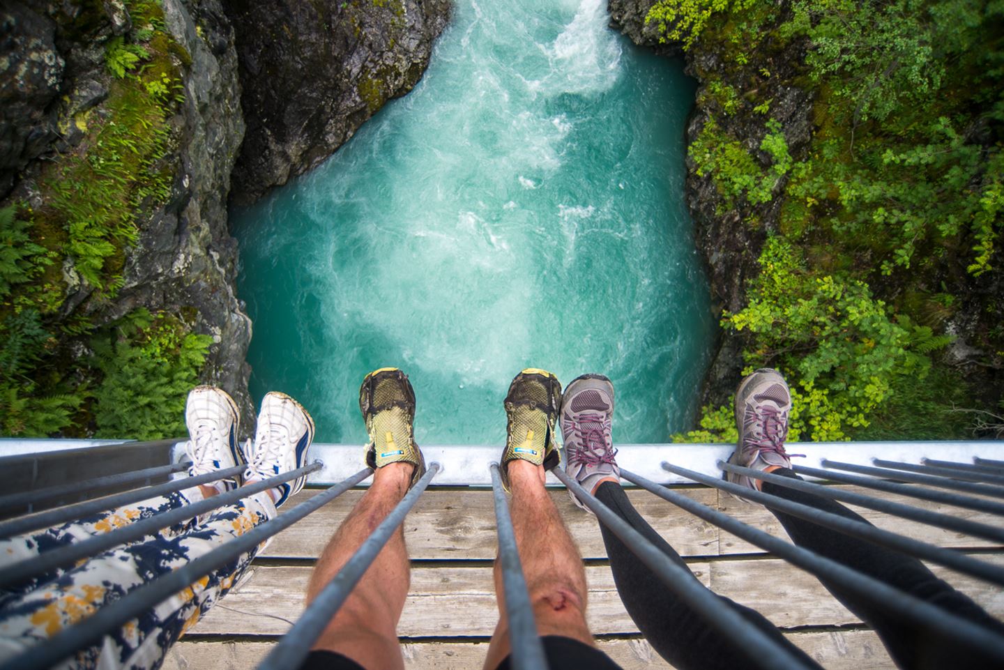 Utsikt frå bru og rett ned i foss med fire par føter med joggesko i framgrunnen.