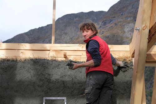 Kvinne lagar vegg av halm og leire