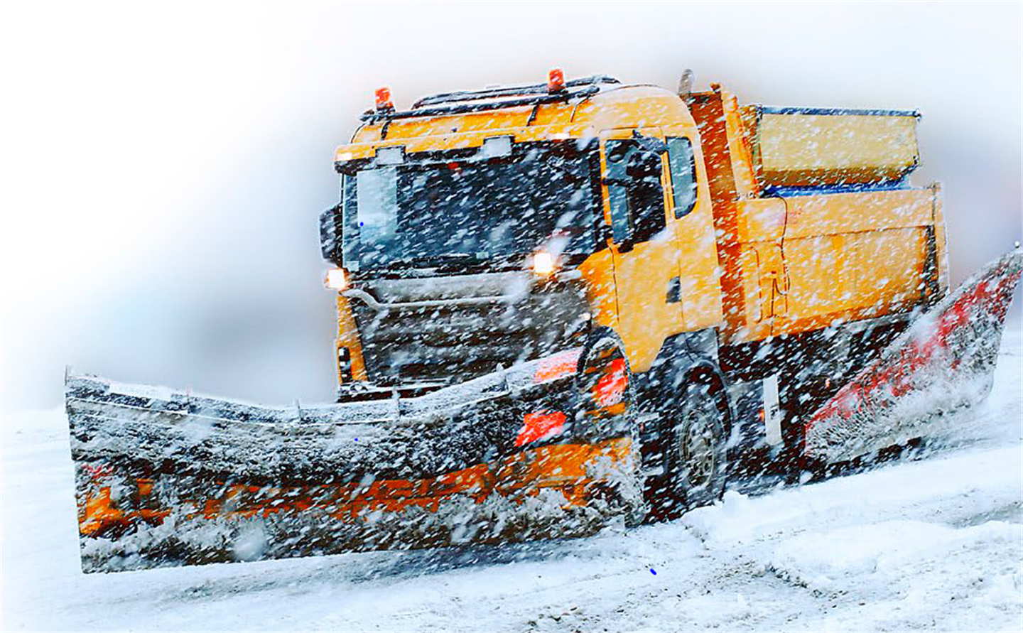 Nærbilde av ein oransje brøytebil i arbeid på veg i tett snødriv vinterstid, snøplogen i front er fremst i bildet. 